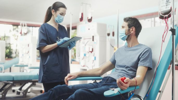 白人男子在光明医院为有需要的人献血。女护士带着平板电脑进来检查供体的进展和健康状况。器官移植病人的捐