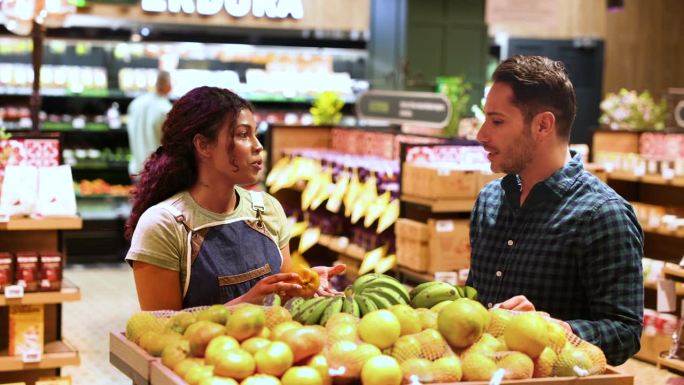 一名拉丁美洲男子在超市的零售店员的帮助下买橘子