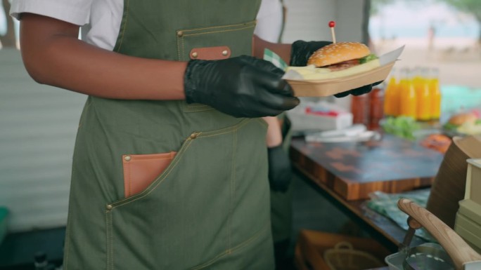 重点是手的女厨师戴着黑色手套，做美味的奶酪肉汉堡送到他们的客户在餐车里。
餐车女工正在为顾客准备汉堡