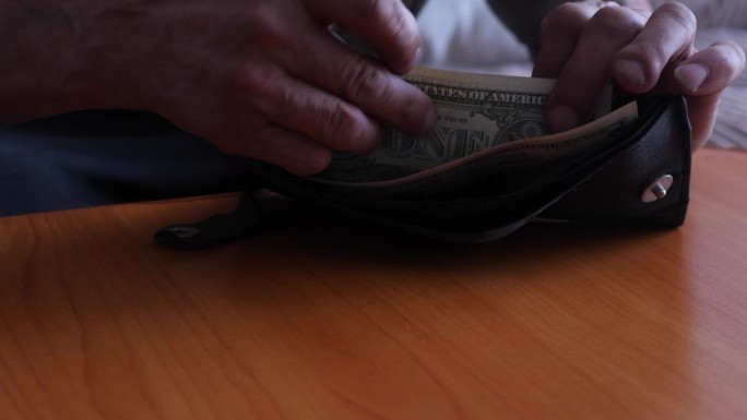一个男人的手打开钱包的特写，里面装着最后的钞票。一个老人的财政开支的概念，在破产的边缘