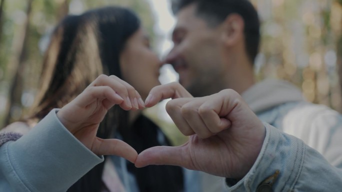 心形符号的特写，用手和模糊的夫妇在户外接吻
