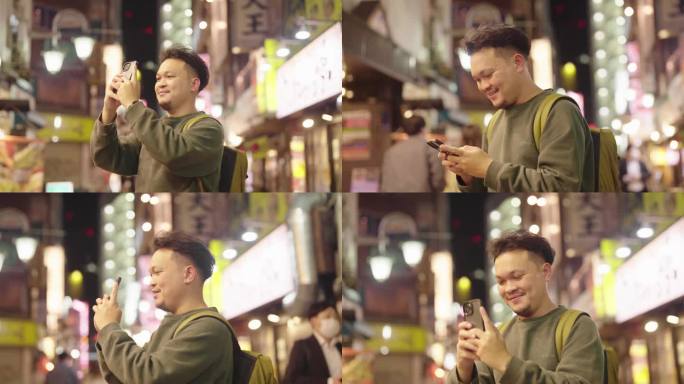 快乐的亚洲背包客在东京的街头夜市里四处走动，他用智能手机拍下了美丽的商店。放松,享受。他微笑着，看起