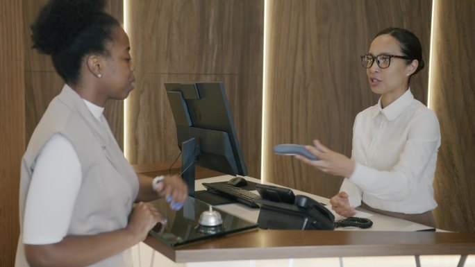 非裔美国女商人与酒店接待员交谈，然后用智能手表付款