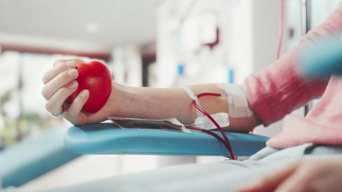 女性献血者的手的特写镜头。白人妇女挤压心形红球，将血液通过管道泵入袋中。器官移植病人的捐赠