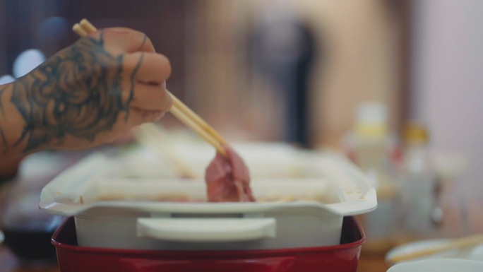亚洲朋友晚上在家聚会时用筷子夹着火锅里的猪肉片。
