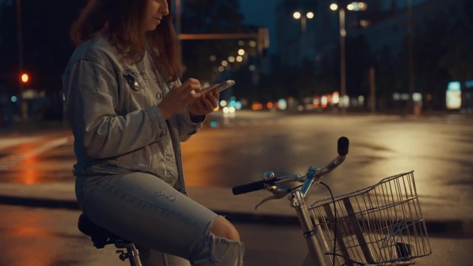 晚上在人行横道上骑自行车拿智能手机的年轻女子