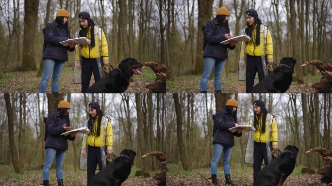 两个年轻女子和狗站在森林里讨论路线，检查纸质地图。白人朋友的肖像，游客选择方向，享受生态旅游与宠物。
