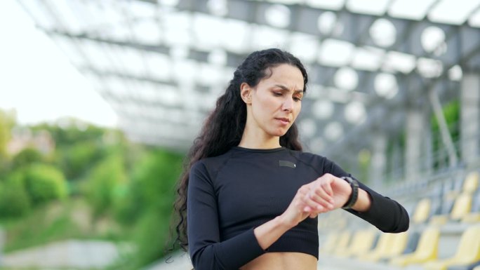 失望的年轻女运动员在城市体育场用智能手表检查训练结果