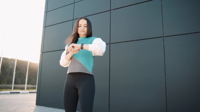 年轻的健身女性在阳光下看智能手表户外运动员健身设备应用技术监控活跃的小工具慢跑者技术慢动作