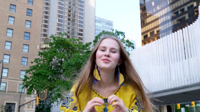 可爱美丽的金发女孩年轻女子看着框架，用她的手做一个心在白绿背景上的黄色衬衫快乐的街头爱和平在乌克兰快
