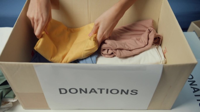 快乐的亚洲少女志愿者在慈善基金会工作时，将衣服产品装入捐赠纸板箱。社工，冠状病毒和隔离。特写镜头。