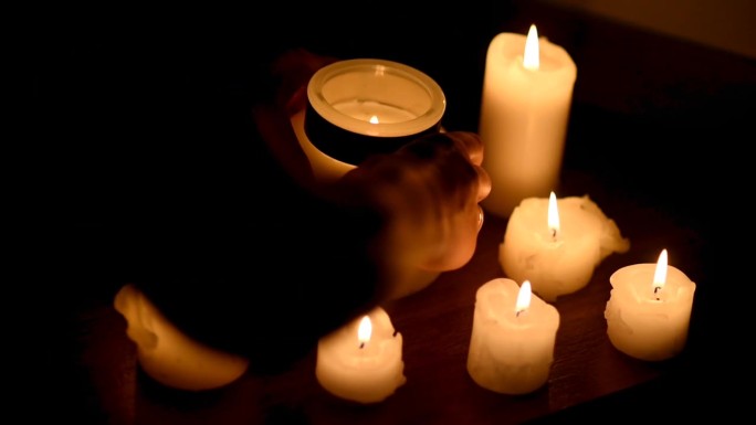 许多燃烧的蜡烛，大小不一。双手将一根大蜡烛放在中间的玻璃罐中。烛光、浪漫或宗教带来的温暖和安慰