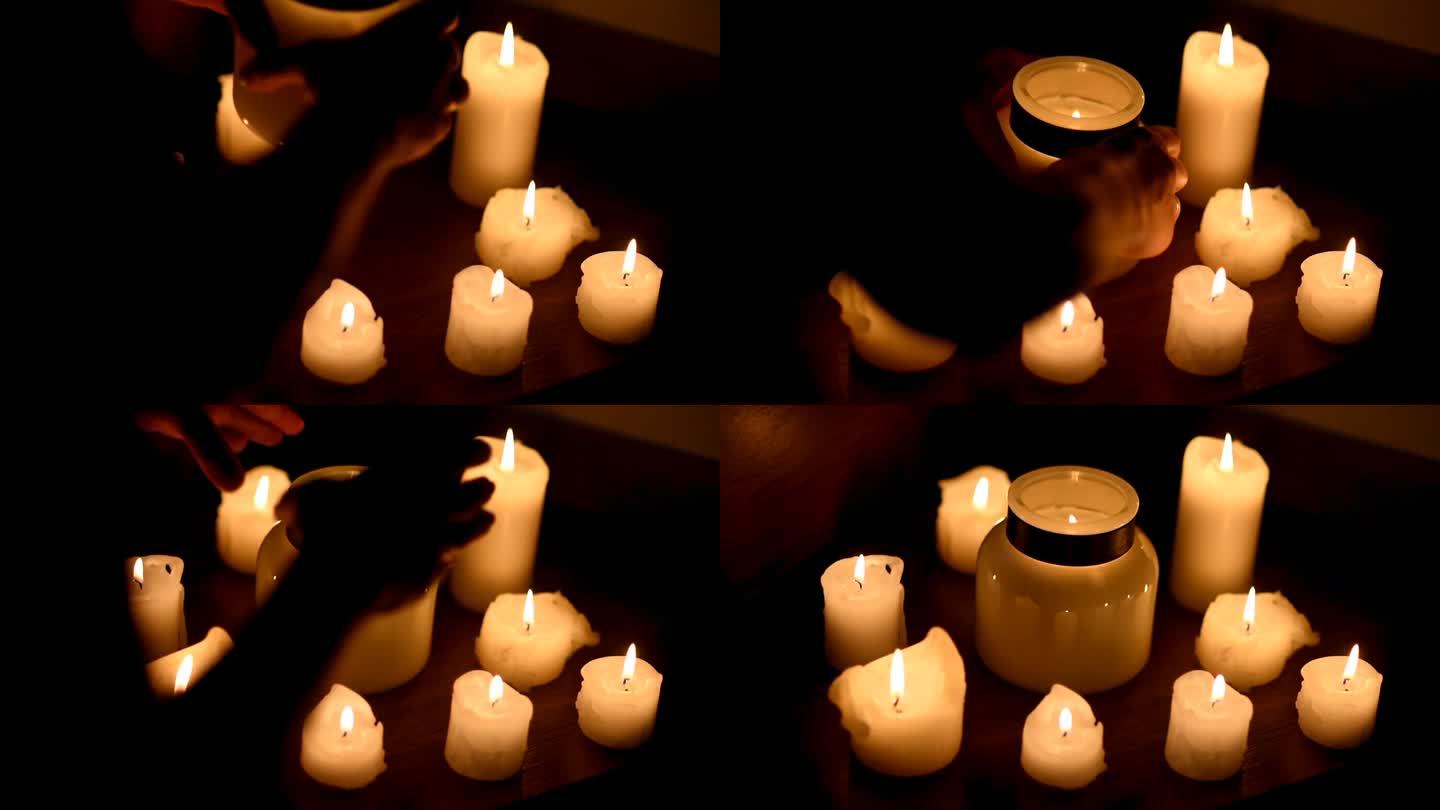 许多燃烧的蜡烛，大小不一。双手将一根大蜡烛放在中间的玻璃罐中。烛光、浪漫或宗教带来的温暖和安慰