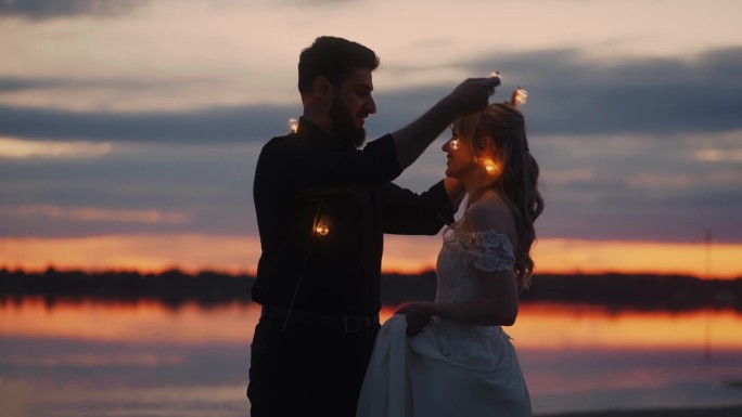 夕阳西下，海岸上一对新婚夫妇的剪影，男子给新娘戴上花环，亲吻她
