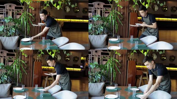 年轻的亚洲服务员在餐厅整理桌子。帅气的男员工穿着深色系带围裙在咖啡馆准备预定的桌子。食品和饮料概念。