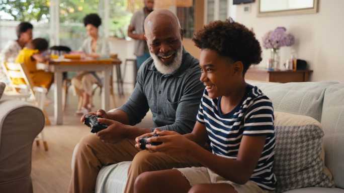 爷爷和孙子坐在家里的沙发上一起玩电子游戏