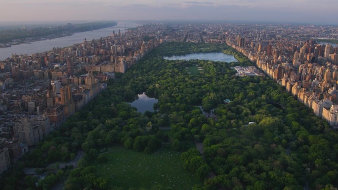 日落时的纽约市景。直升机航拍画面。曼哈顿岛中央公园周围的现代摩天大楼。关注城市公园里的自然、树木和湖