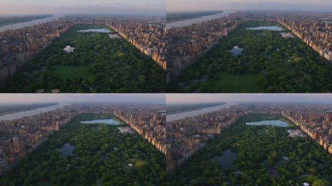 日落时的纽约市景。直升机航拍画面。曼哈顿岛中央公园周围的现代摩天大楼。关注城市公园里的自然、树木和湖