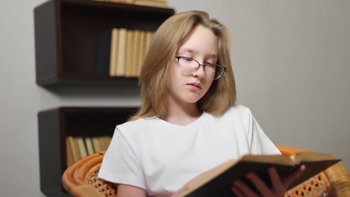 一个十几岁的女孩正在一把竹椅上看书。
