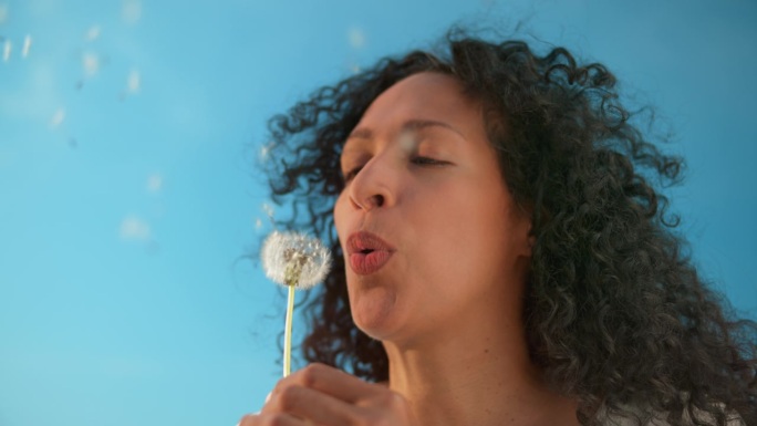 女人在阳光下吹走蒲公英的种子