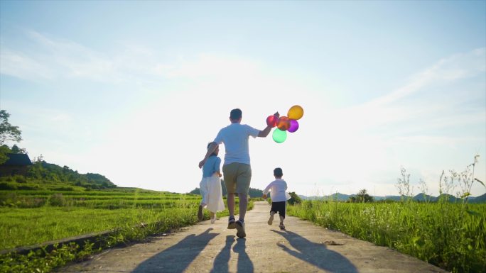 一家三口拿着彩色气球逆光奔跑幸福家庭温馨