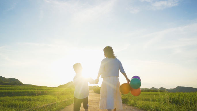 妈妈牵着孩子户外慢步亲子逆光背影温馨家庭