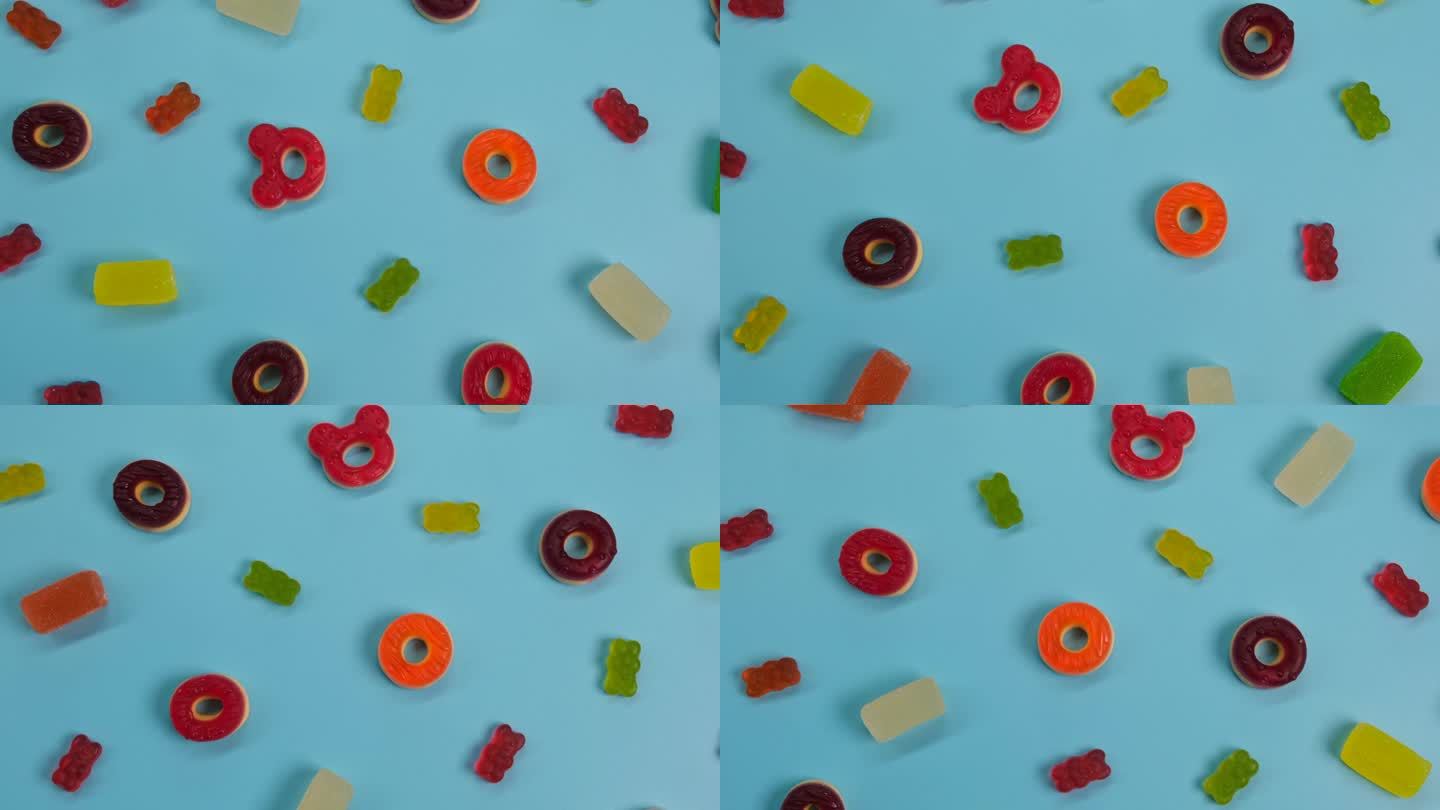 旋转背景的各种果冻糖果，熊，甜甜圈，糖果，糖果，糖霜，在蓝色背景上的特写顶视图概念生日聚会或庆祝活动