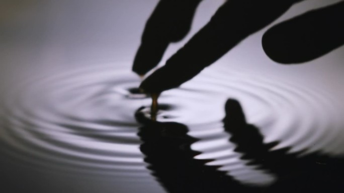 一只女性手的剪影轻轻地触碰水面，在水面上形成圆圈。