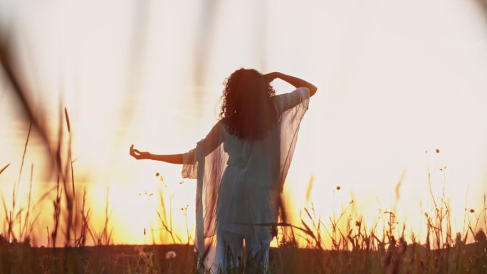 一个女人站在草地上，在日落时跳舞