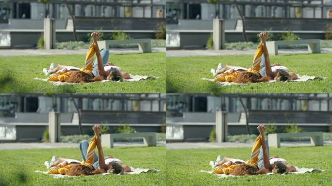 女人，朋友和躺在草地上手牵手在公园暑假，休息或周末在城市。妇女们在野餐垫子上或阳光下的田野上放松，在