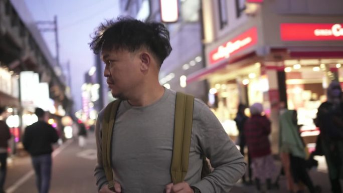 亚洲男子背包客走在繁忙的街道夜市，抬头看/东京，日本。