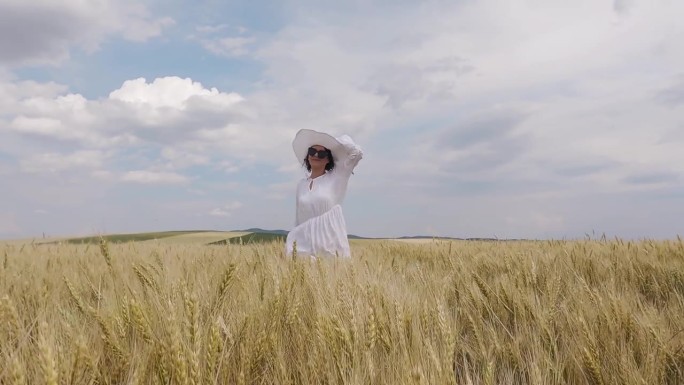穿着白衣服、戴着白帽子的快乐女人在麦田里奔跑，慢动作