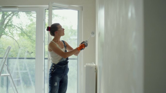年轻女子用油漆滚筒刷着她梦想中的房子墙壁