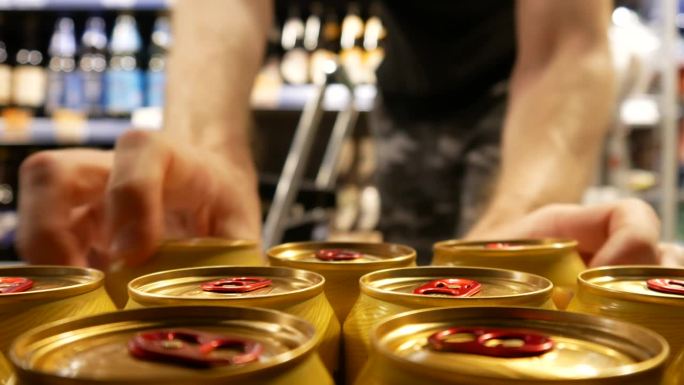 超市里许多漂亮的金色啤酒罐的特写镜头，一个买家拿了三个，把它们放进购物车