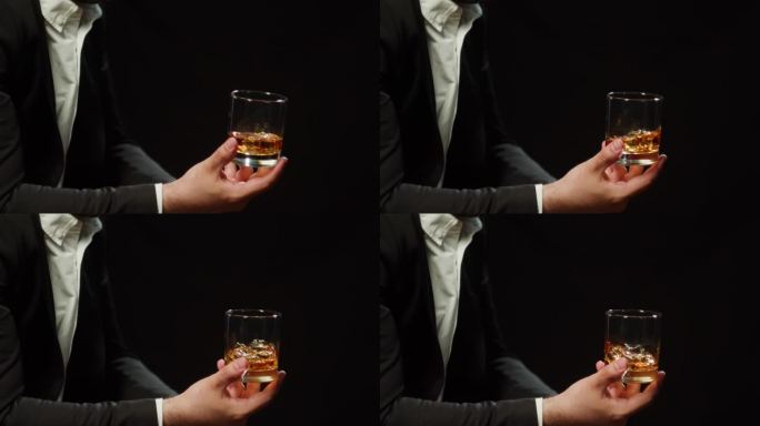 喝白兰地或威士忌的特写镜头。富人喝着黑色背景的豪华干邑。酒精琥珀朗姆酒，酒精饮料在玻璃。