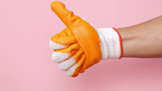 橙色的机械手套在粉红色的背景上做了一个很棒的大拇指标志。