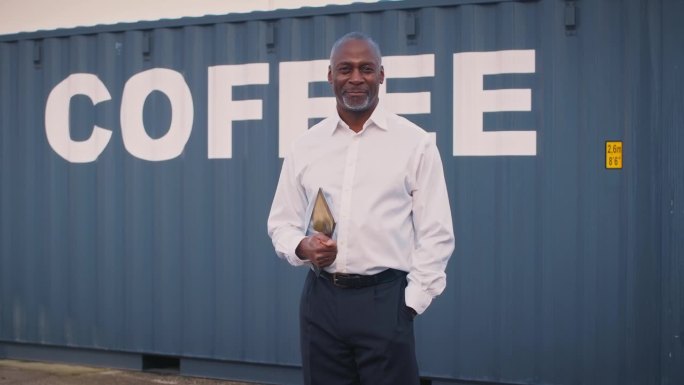 一名男性货运经理手持数码平板电脑站在装咖啡的集装箱旁