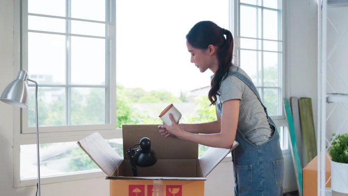 有魅力的亚洲女性在休闲布手移动纸板箱纸箱家庭搬迁新房子在新公寓，房子装修亚洲女性移动家具家居用品在客