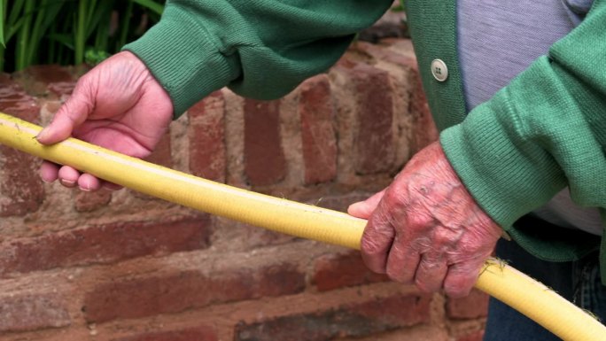 一位老人手持一根花园软管，将水浇在绿色的植物上。侧视图，特写。高品质4k画面