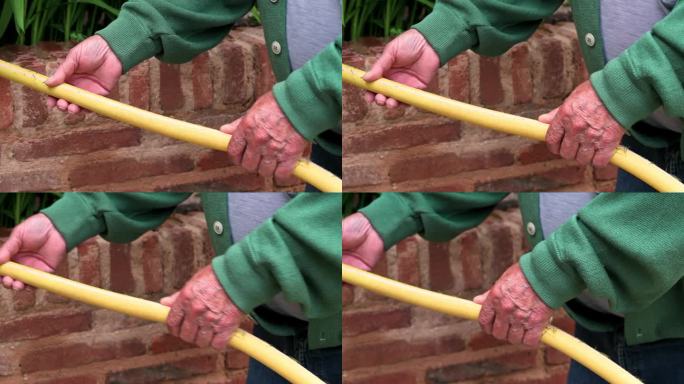 一位老人手持一根花园软管，将水浇在绿色的植物上。侧视图，特写。高品质4k画面