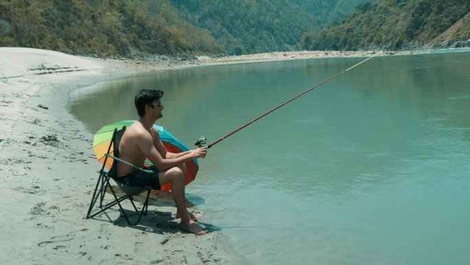 光膀子的游客坐在折叠椅上在湖里钓鱼