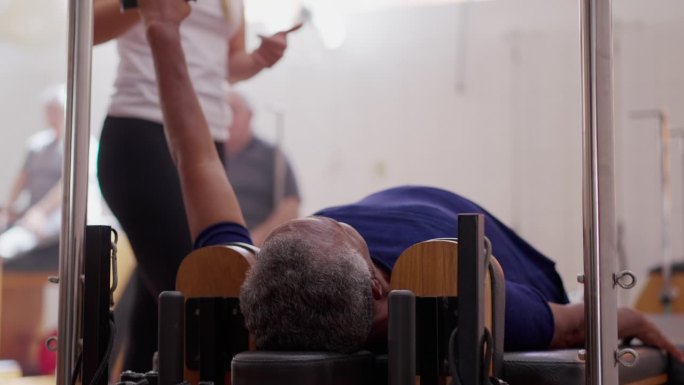 使用普拉提机的人，由普拉提女教练指导，理疗工作室，脊柱健康锻炼
