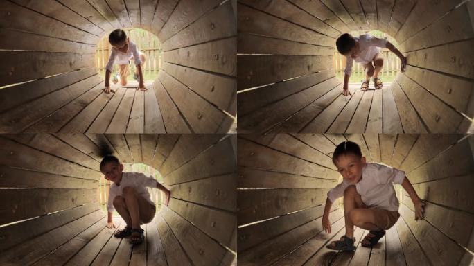 小男孩爬过操场上的木制隧道或管道。孩子们在户外玩耍，孩子们玩得开心，暑假和假期