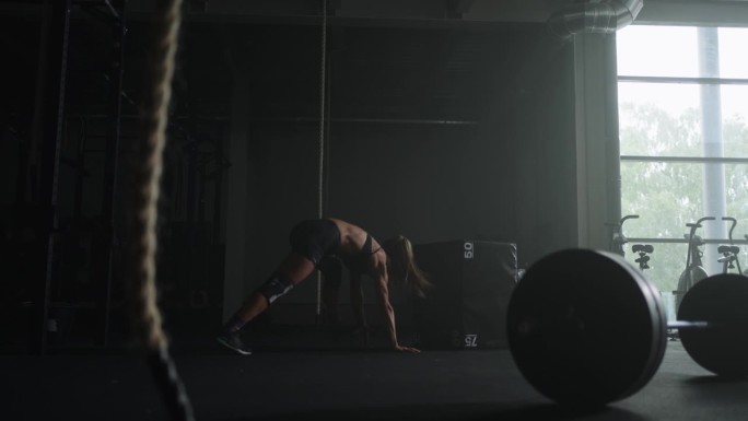 有动力的女运动员在健身房单独训练，女健美运动员跳跃和做俯卧撑