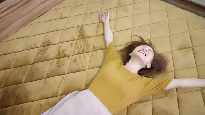 高角度中手持拍摄一张金色天鹅绒格子羽绒被的大床，一个快乐的亚洲女人舒适地躺在床上