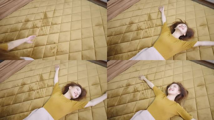高角度中手持拍摄一张金色天鹅绒格子羽绒被的大床，一个快乐的亚洲女人舒适地躺在床上