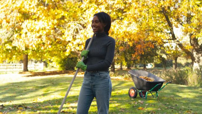 在花园里干活的妇女画像，把秋叶扫进手推车