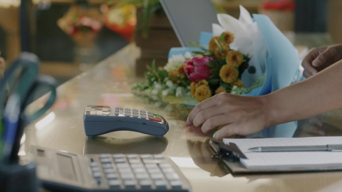 用信用卡付款的手购买一束花的特写镜头和柜台前使用终端的女售货员