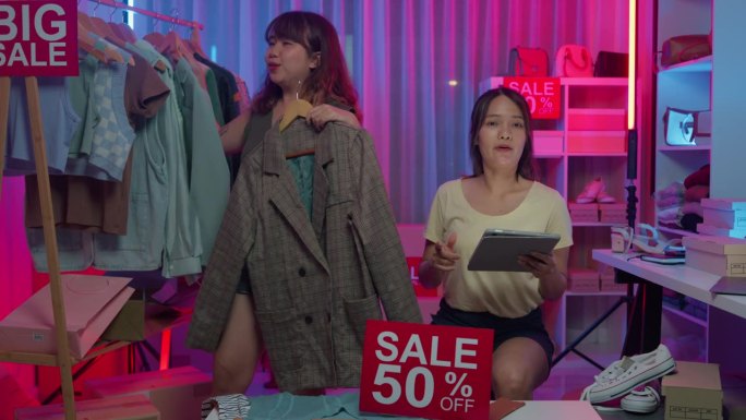 年轻的亚洲女性在晚上通过手机直播向商店里的顾客展示最新的时装系列。中小企业小企业电子商务。