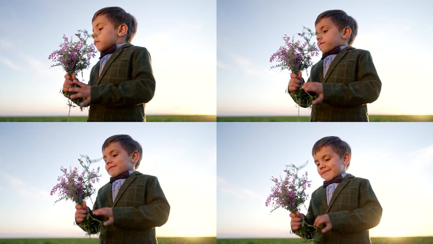 可爱的小男孩的肖像在节日服装与蝴蝶和花束在开放地区的田野背景。孩子，帅儿子带花，节日概念。日落时间。